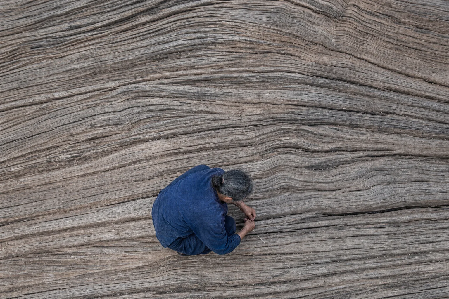 A woman repairing a narrow split in a weathered wood surface